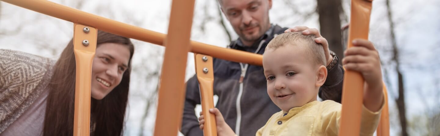 Headerbild: Eltern betrachten ihr spielendes Kind auf dem Spielplatz