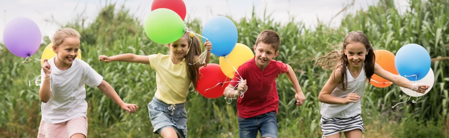 Headerbild: Eine Gruppe junger Schüler*innen läuft mit Luftballons auf einer Wiese