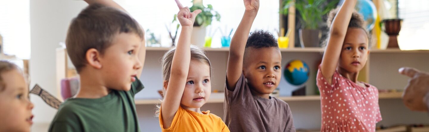 Headerbild: Gruppe von Kindern in der Kita zeigen die Zahl 2 mit ihren Fingern