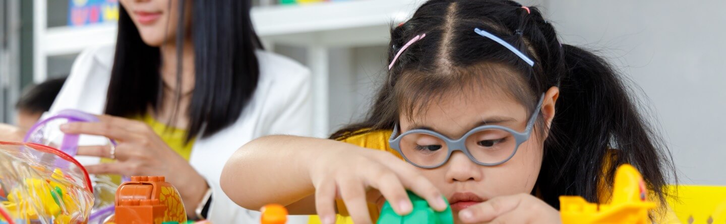 Headerbild: Mädchen mit Brille spielt freudig mit buntem Spielzeug