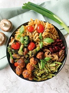 Foto eines Tellers mit Nudeln und Gemüsebällchen. Daneben liegen Champignons und Frühlingszwiebeln.